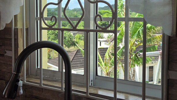Un baño con ventana, un grifo y vistas a una zona residencial con casas y vegetación.