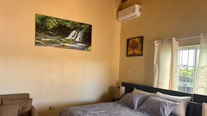 Un dormitorio con cama, una silla, un cuadro de una cascada y una ventana con cortinas.
