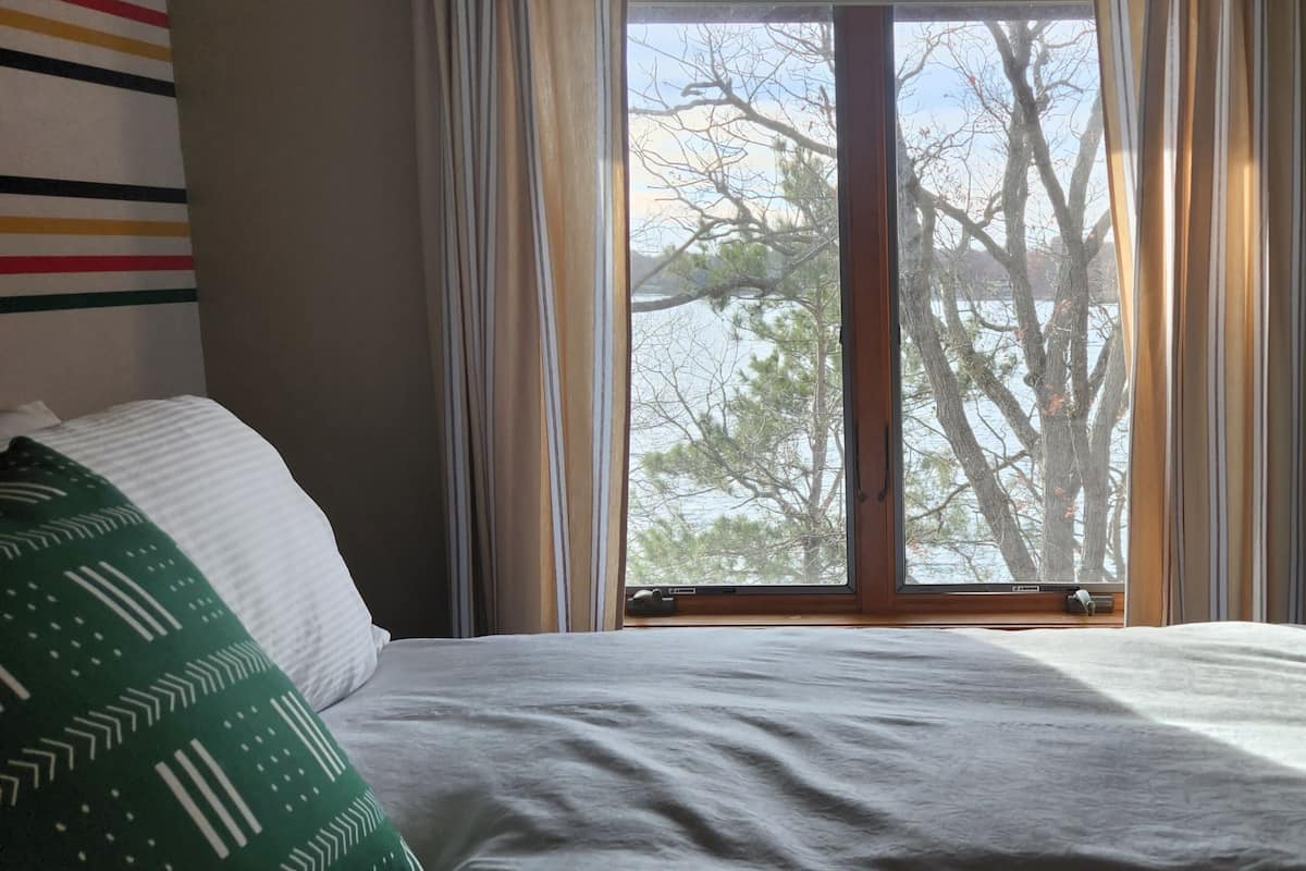 A bedroom with a bed, a window with curtains, and a view of trees outside.