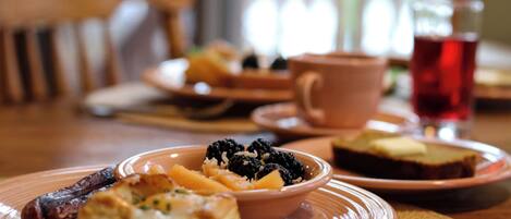 A dining table with plates of food, including a bowl of fruit and a cup of tea.