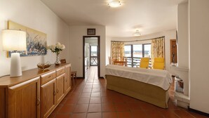 Quarto espaçoso com cama grande, um armário de madeira, uma mesa com cadeiras e vista pela janela.