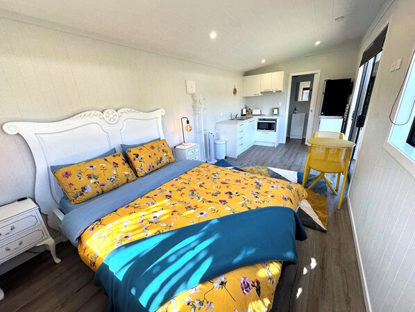Cozy retreat with a neatly made bed, bedside table, and window offering a view of the adjacent kitchen area.