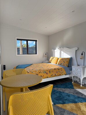 Relax in this serene bedroom with a large bed, a small table, and a window offering a view of lush greenery.