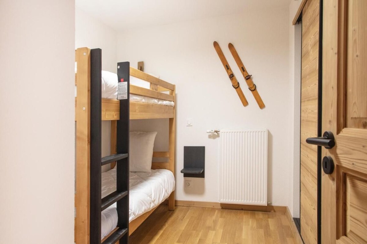 Una habitación pequeña y funcional con una cama litera, un radiador y esquíes colgados en la pared.