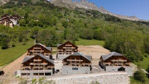 A mountain lodge with multiple wooden buildings, a stone pathway, and a view of the surrounding mountains.
