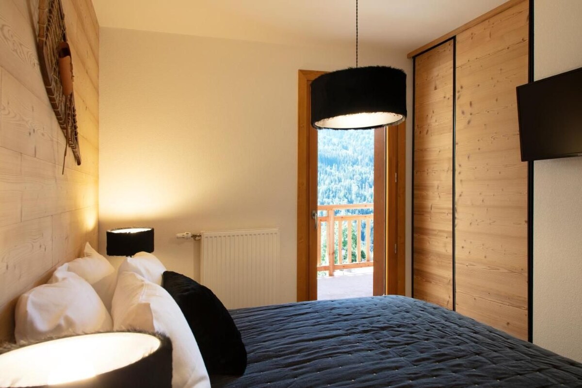 Un dormitorio con cama, mesita de noche, lámpara y vistas a un balcón con barandilla de madera.