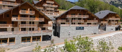Una cabaña de varios pisos con balcones, paredes de piedra y un paisaje montañoso de fondo.
