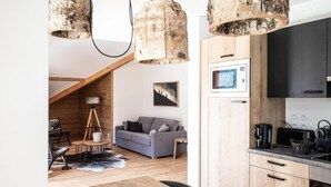 A cozy interior with a wooden dining table, a gray sofa, and a kitchen area with modern appliances.