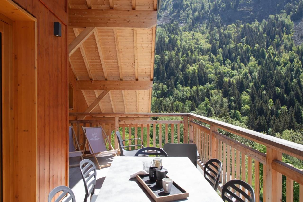 Una terraza de madera con una mesa y sillas, con vistas a un valle boscoso.