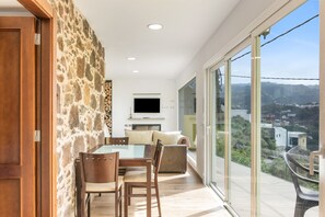 En modern inredning med en vägg av sten, en matplats med ett glasbord och en stor skjutdörr i glas som leder ut till en balkong med utsikt över staden.