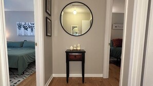 Un pasillo con piso de madera, un espejo redondo en la pared y una pequeña mesa con velas.