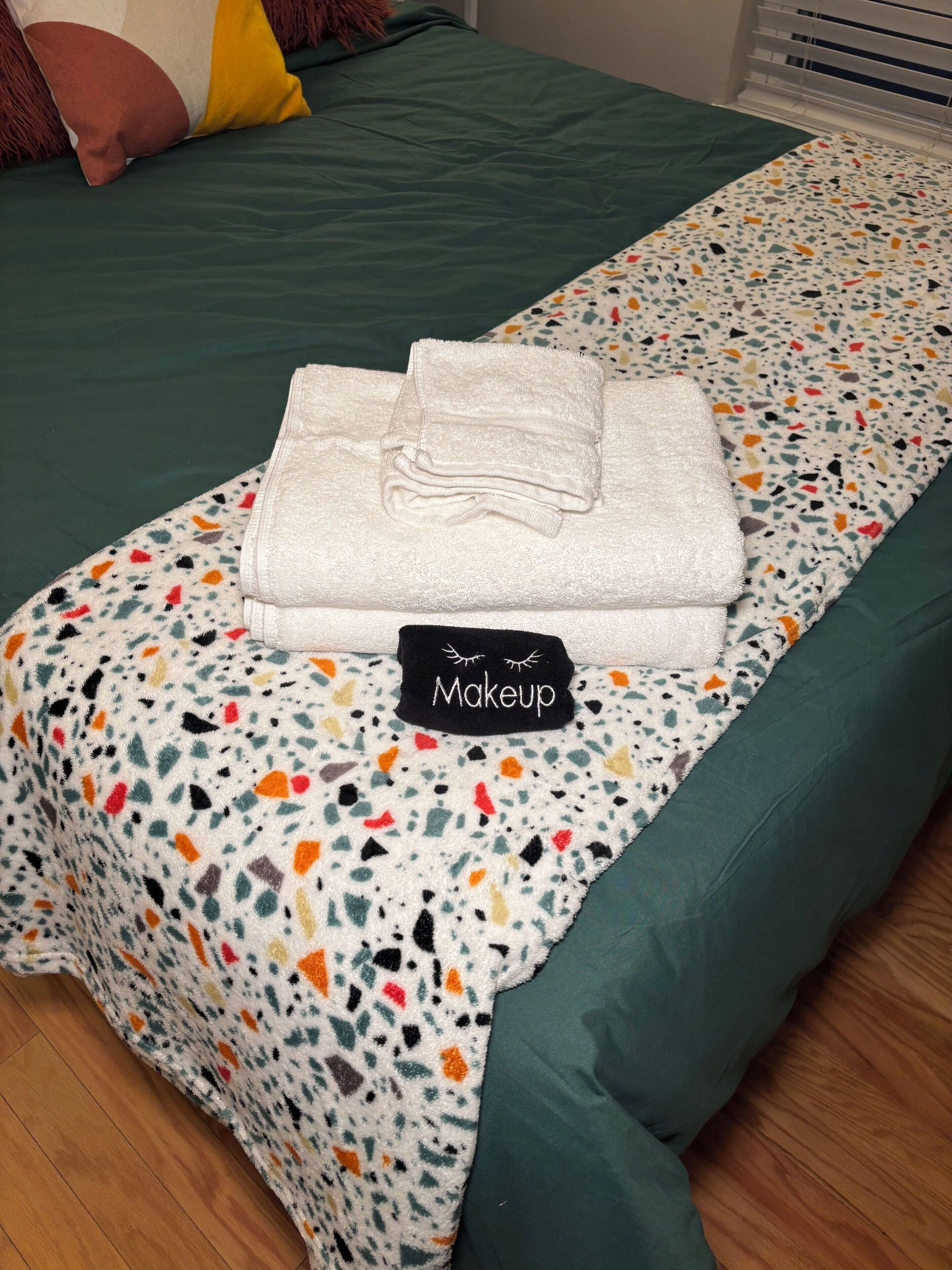 Un lit bien fait, recouvert d’une couverture verte et d’un plaid coloré à motifs.