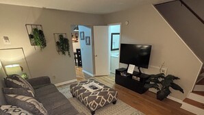 Una sala de estar con un sofá modular, un reposapiés y un televisor sobre un mueble.