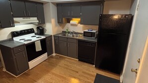Una cocina compacta con armarios oscuros, una estufa blanca, un refrigerador negro y un microondas.