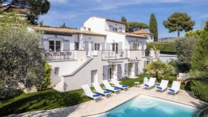 A white villa with a swimming pool, sun loungers, and a well-maintained garden.