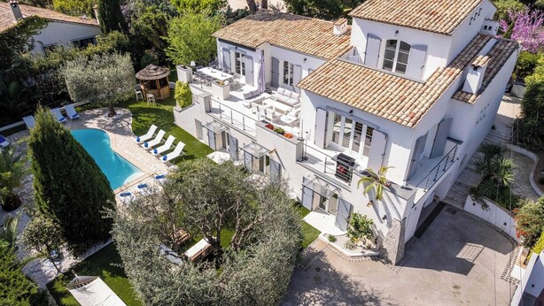 A large, two-story house with a swimming pool, outdoor seating, and a well-maintained garden.