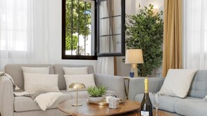 Un salon avec un canapé gris, une table basse ronde en bois, une plante en pot, une bouteille de vin et une lampe.