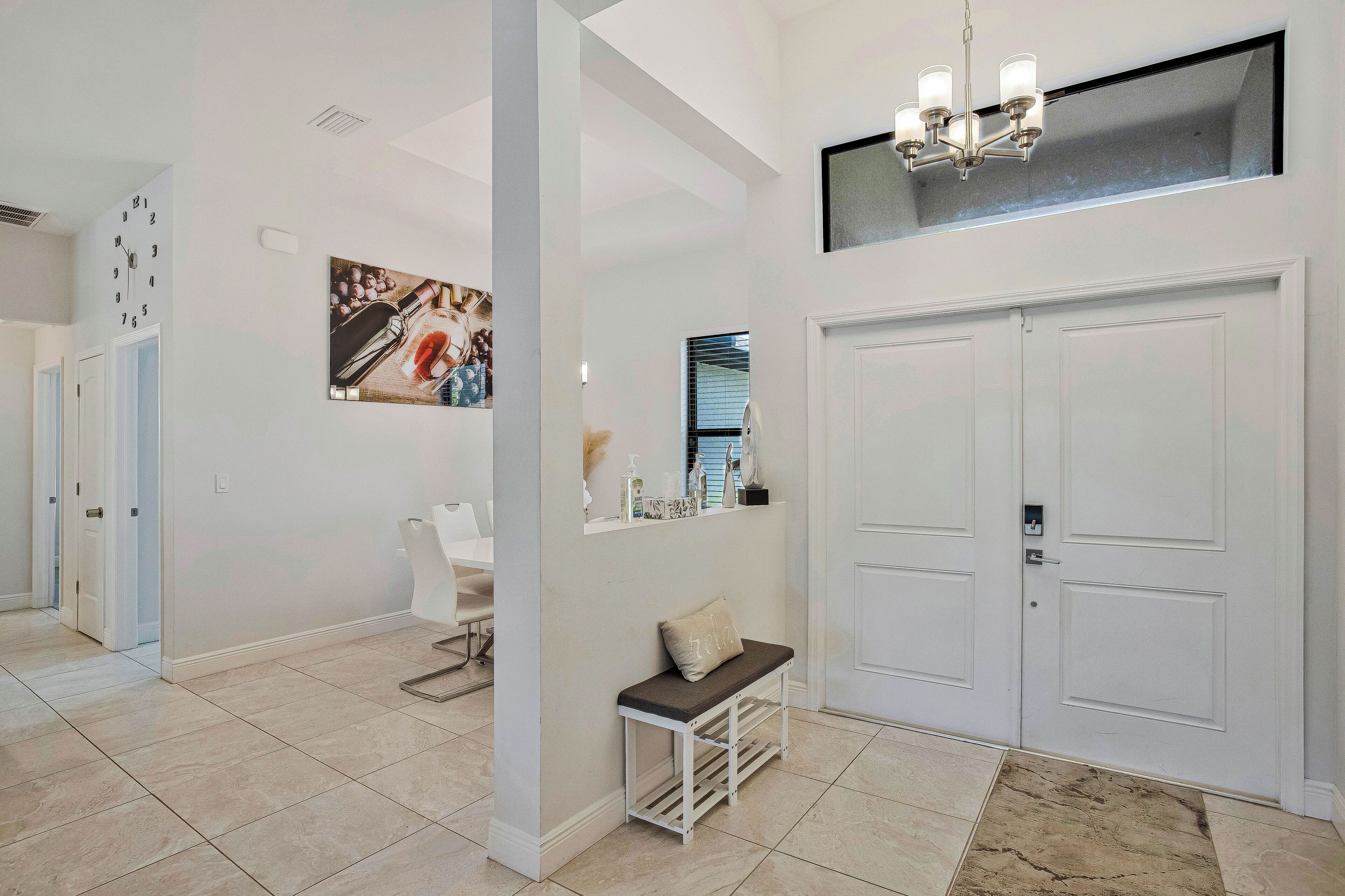 A hallway with a bench, a clock, and a chandelier.