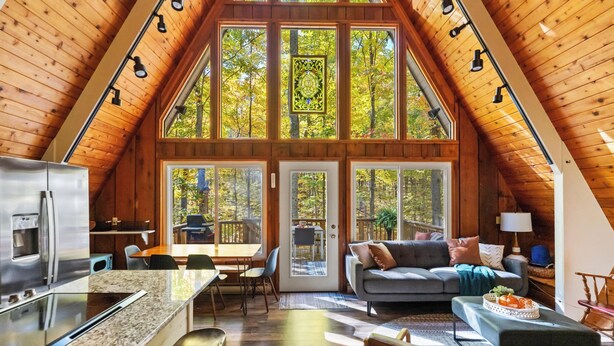 A spacious loft with a high ceiling, a kitchen area, a dining space, and a cozy living area with a sofa and a fireplace. - 4BR A-Frame at Schuss Mtn | Torch Lake & Pool Access l Sleeps 11 (Bellaire)