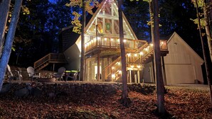 A cabin with a glass front, wooden deck, and a stone foundation. - 4BR A-Frame at Schuss Mtn | Torch Lake & Pool Access l Sleeps 11 (Bellaire)