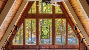 A room with a sloped ceiling, wooden beams, and large windows with a stained glass window in the center. - 4BR A-Frame at Schuss Mtn | Torch Lake & Pool Access l Sleeps 11 (Bellaire)