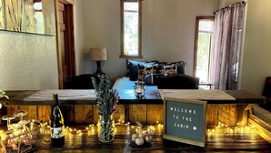 A cozy cabin interior with a wooden bench, a welcome sign, a lamp, and a vase with flowers. - Welcome to Mountain Greens Cabin (Grants Pass)