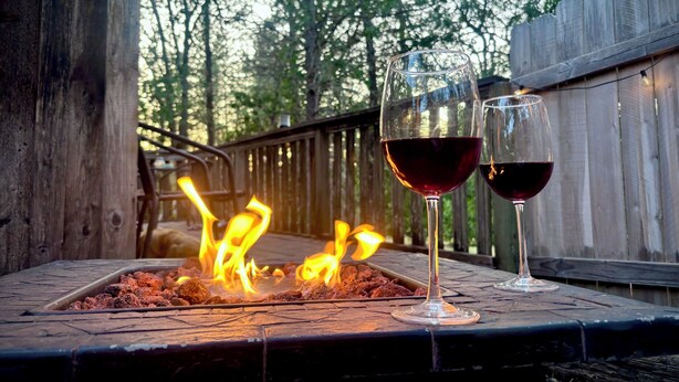 A fire pit with two glasses of red wine on a wooden deck surrounded by a wooden fence and trees. - Welcome to Mountain Greens Cabin (Grants Pass)