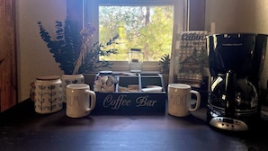 A coffee bar setup with two mugs labeled "Coffee Bar" and "Comfort," a coffee maker, and a window with a view of trees. - Welcome to Mountain Greens Cabin (Grants Pass)
