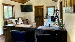 A cozy room with a wooden ceiling, a flat-screen TV mounted on the wall, a dining table with chairs, and a kitchen area with a sink and cabinets. - Welcome to Mountain Greens Cabin (Grants Pass)