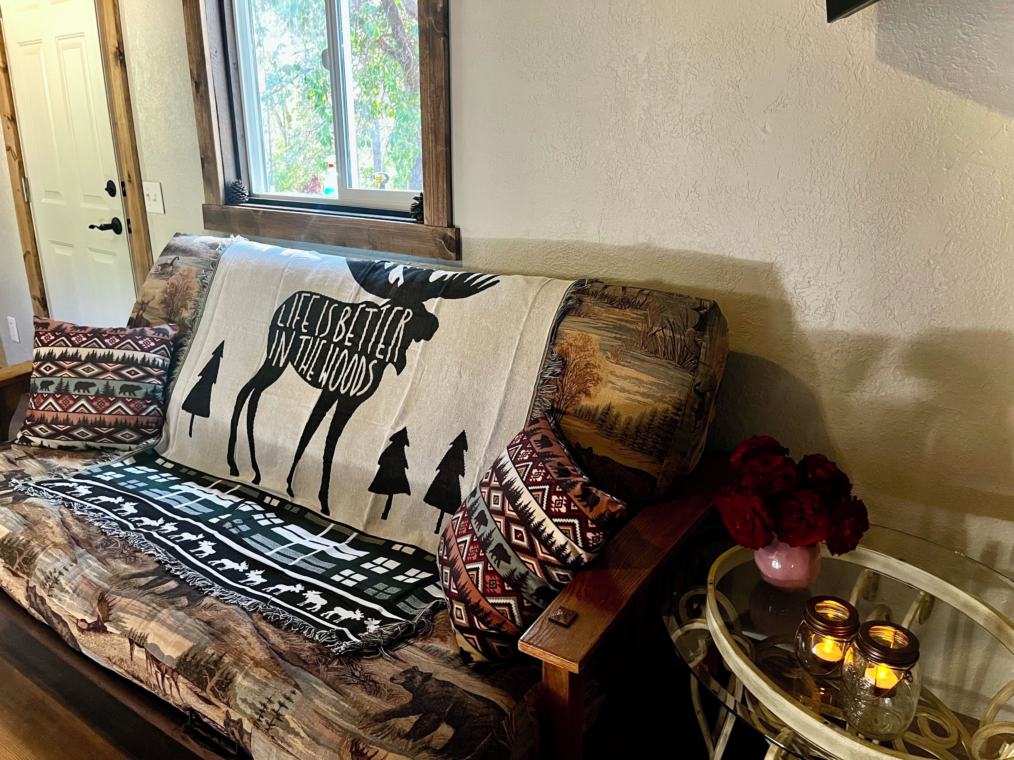 Ein gemütliches Wohnzimmer mit einer Couch, verziert mit gemusterten Kissen, einem Fenster mit Blick auf Bäume und einem kleinen Tisch mit Kerzen.