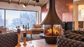 Un salon chaleureux avec une grande cheminée, des sièges confortables et une vue sur l’extérieur.
