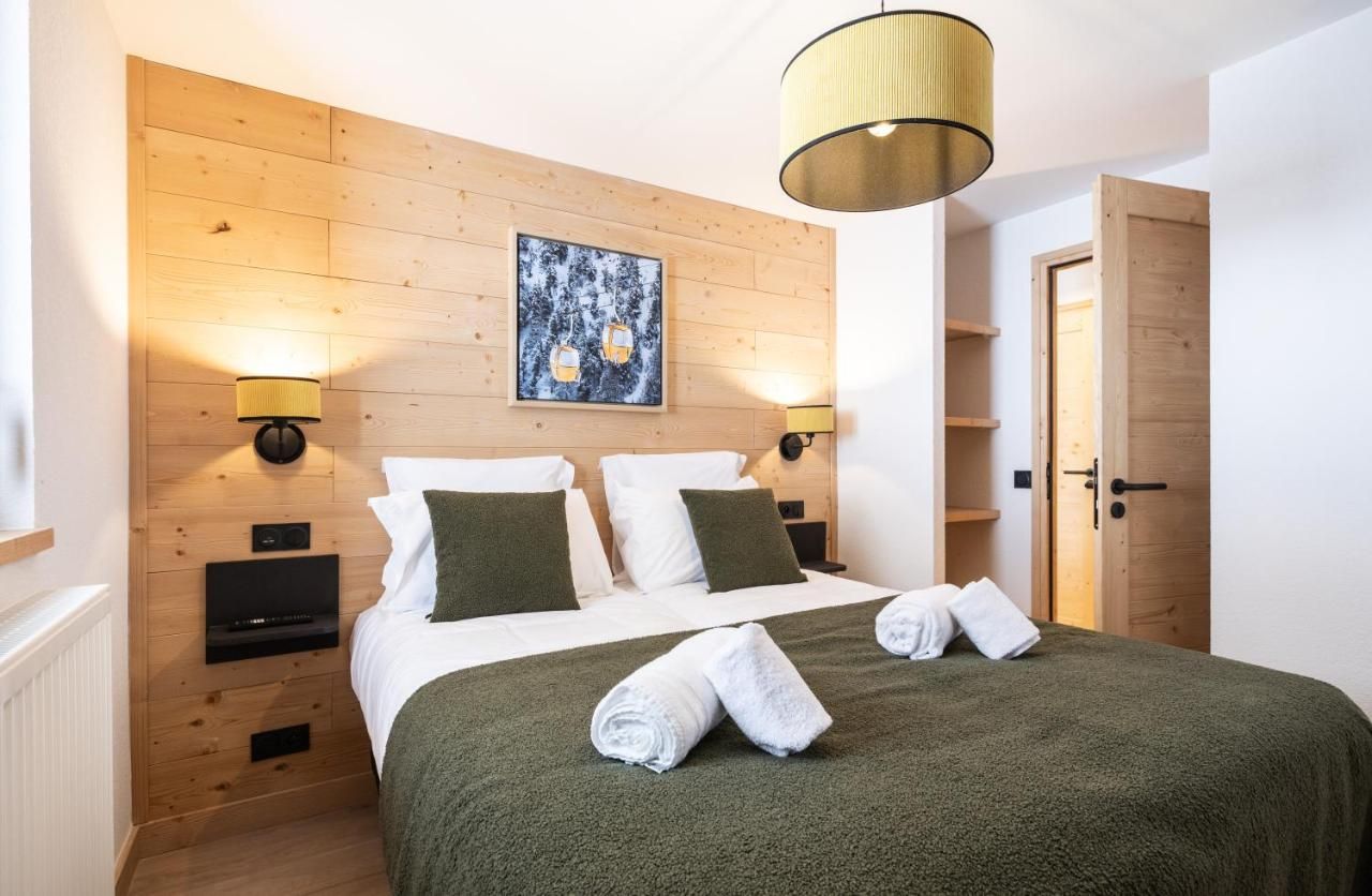 Ein Hotelzimmer mit einem hölzernen Kopfteil, zwei Nachttischen mit Lampen, einem Bett mit grüner Bettwäsche und einem Gemälde an der Wand.