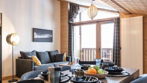 A dining area with a wooden table set for a meal, a sofa with cushions, a floor lamp, and a window with curtains.