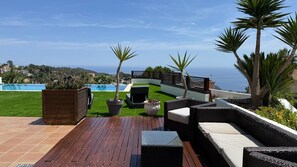 A deck with outdoor furniture, a pool, and a view of the sea.