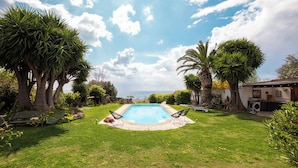 Ein Garten mit Swimmingpool, umgeben von Palmen und Blick aufs Meer.