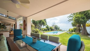Ein Essbereich mit einem Glastisch, blauen Kissen und Blick auf Pool und Garten.