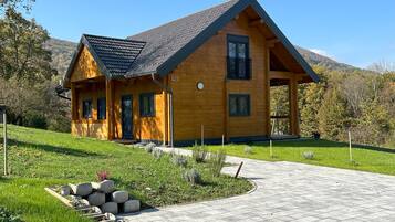 A wooden house with a sloped roof, a paved driveway, and a grassy yard.