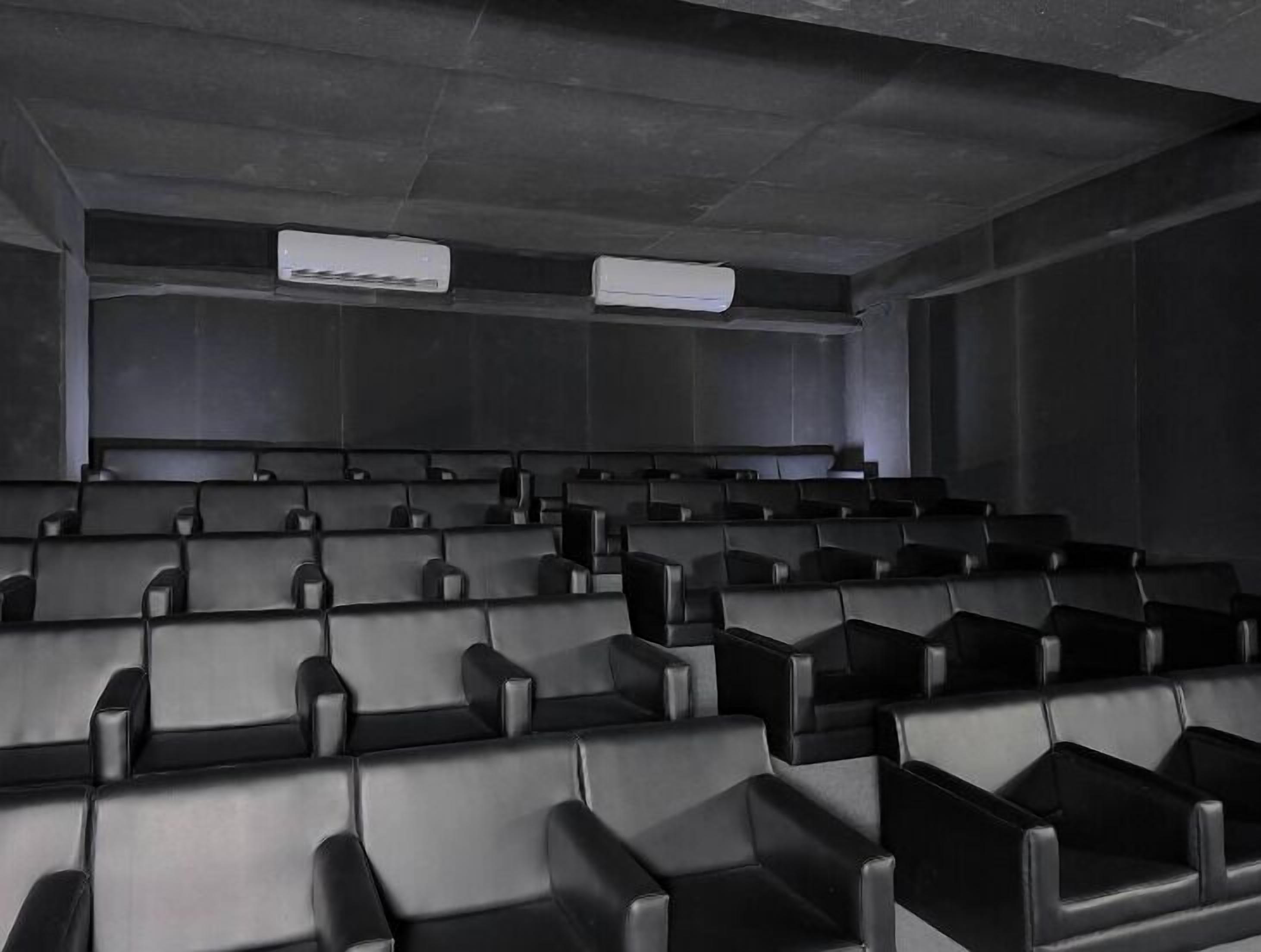 Cine con hileras de butacas de cuero negro y unidades de aire acondicionado en el techo.