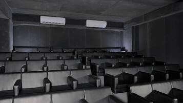 Cine con hileras de butacas de cuero negro y unidades de aire acondicionado en el techo.