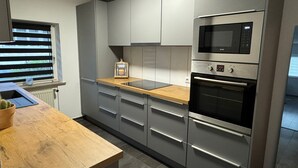 Et moderne køkken med grå skabe, en træbordplade, indbygget mikroovn og en stålfarvet ovn.