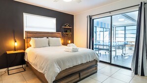 Ein modernes Hotelzimmer mit einem großen Bett, einem Nachttisch mit Lampe, einer runden Wanddekoration und Blick auf den Balkon.