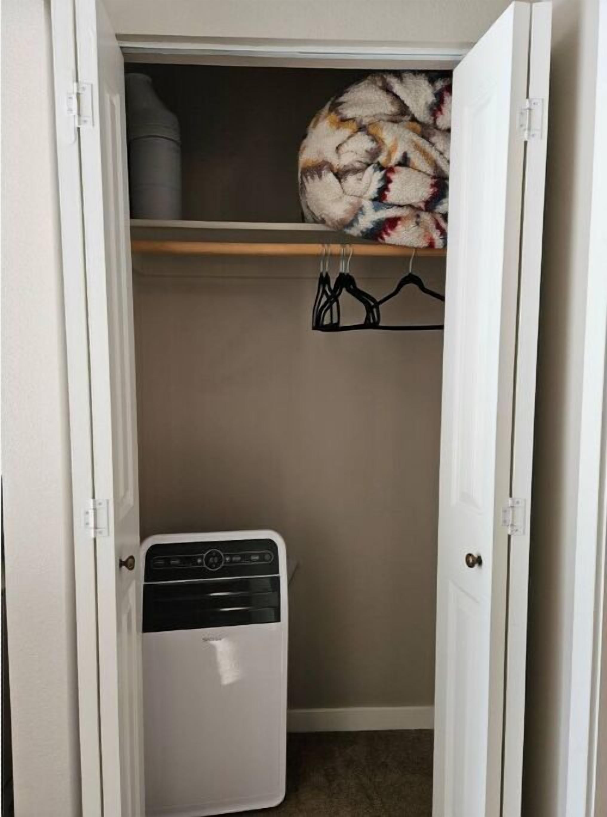 A compact room with a white heater, a hanging coat rack, and a closet with a patterned rug.