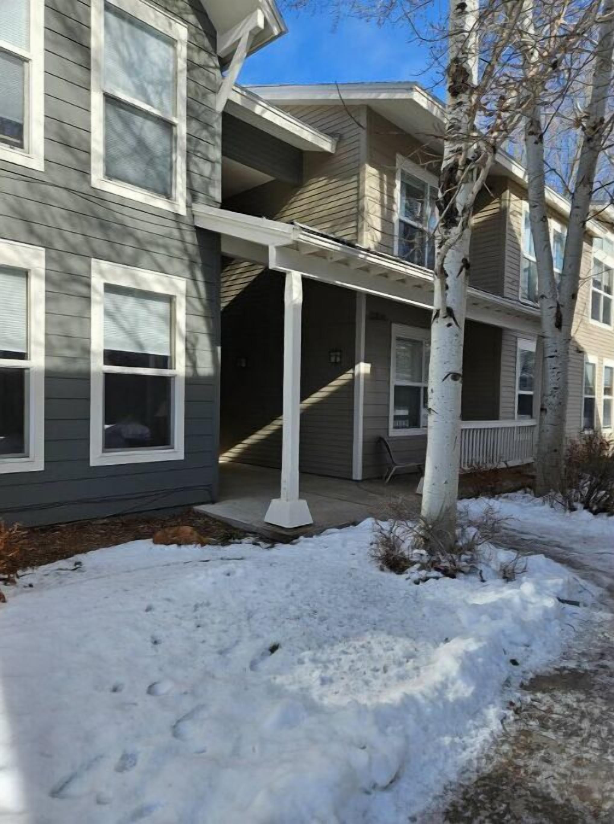 A multi-story residential building with a covered porch and a snow-covered ground.