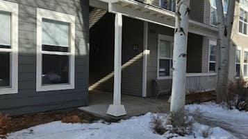 A multi-story residential building with a covered porch and a snow-covered ground.
