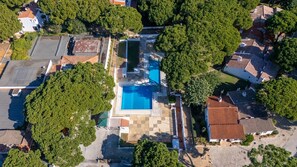 Vue aérienne d’un quartier résidentiel avec une piscine entourée d’arbres et de maisons aux toits en tuiles.