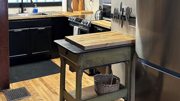 Uma cozinha com mesa de madeira, eletrodomésticos de aço inoxidável e um relógio na parede.