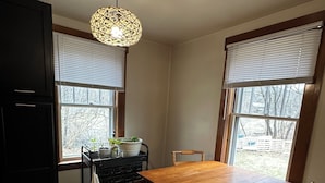 Uma cozinha com mesa e cadeiras de madeira, luminária pendente e janela com persianas.