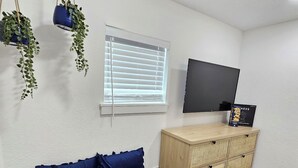 A room with a wooden bench, a blue cushion, a wooden cabinet, and hanging plants. - Crashpads (Orlando)