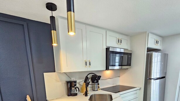 A modern kitchen with white cabinets, stainless steel appliances, a bar stool, and a pendant light. - Crashpads (Orlando)