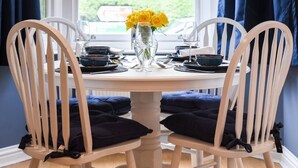 A round dining table with white chairs and dark cushions, set with dinnerware and a vase of yellow flowers.